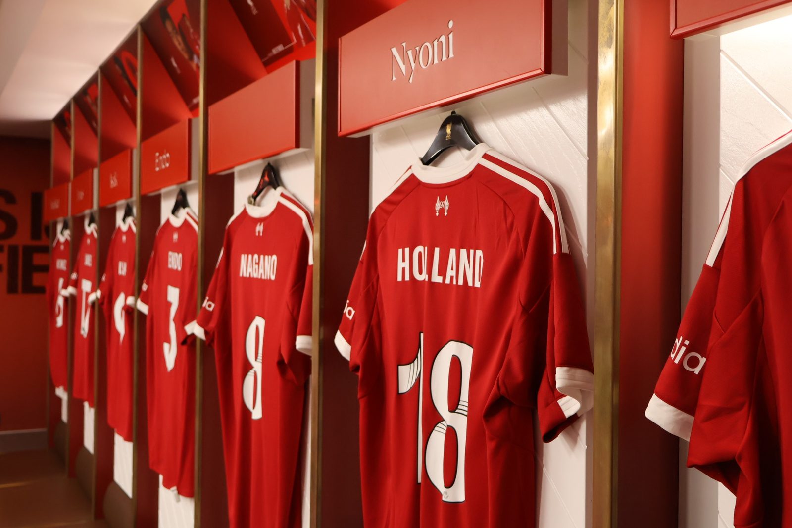 Vestiar la Liverpool FC: tricouri roșii expuse pe umerașe, atmosferă de stadion.